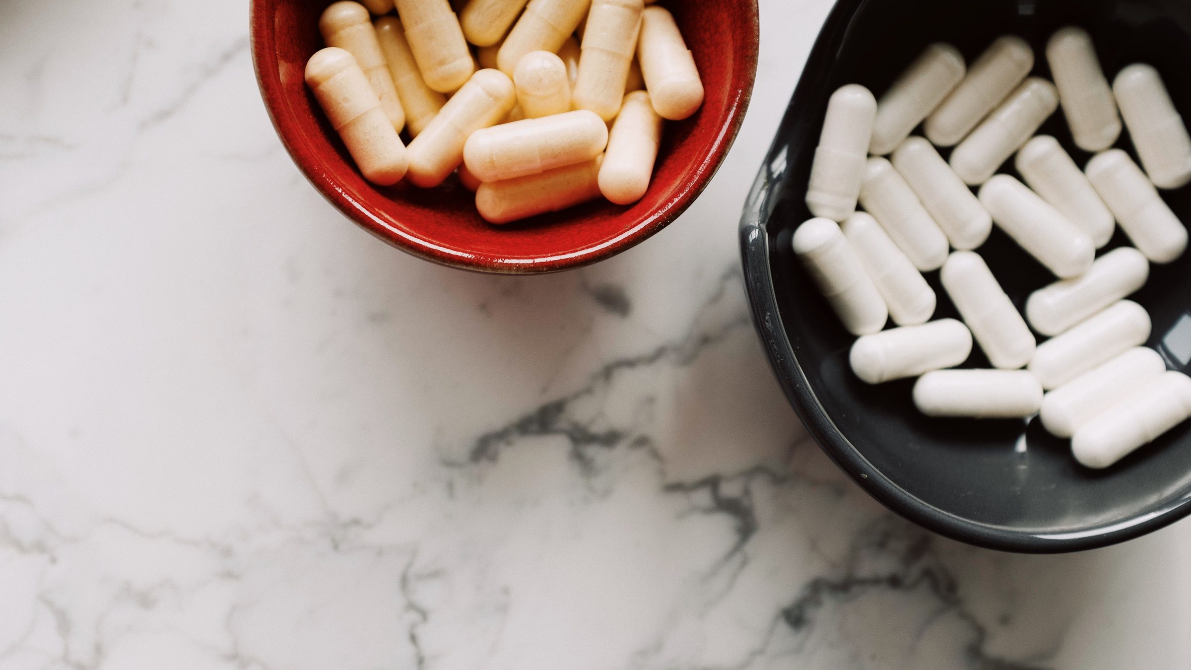Cream and white supplement capsules in two bowls on a marble surface